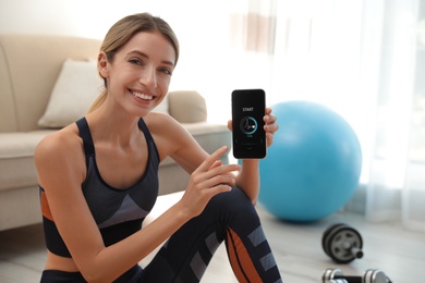 Photo of Young woman showing smartphone with fitness app at home