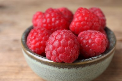 Tasty ripe raspberries in bowl on wooden table, closeup