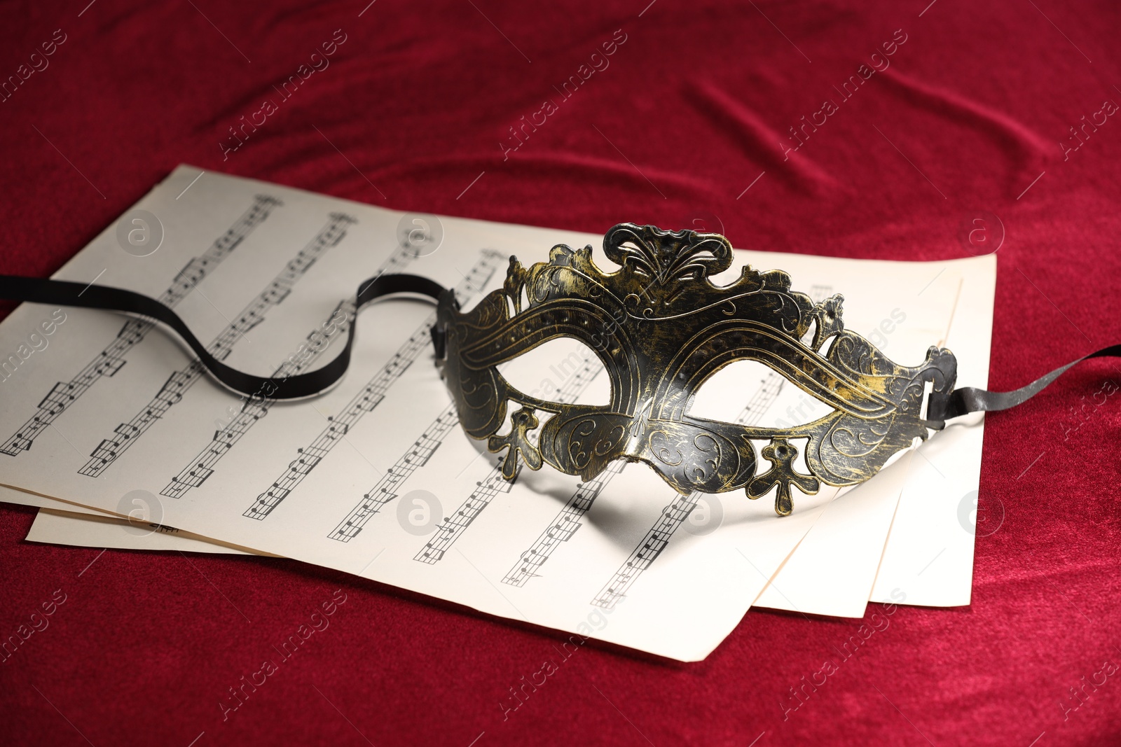 Photo of Elegant face mask and music sheets on red fabric. Theatrical performance