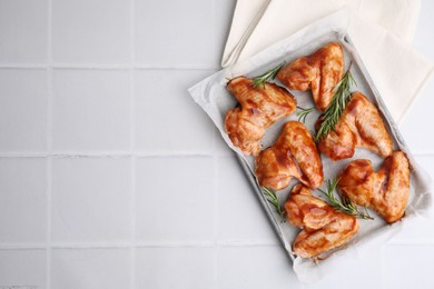 Photo of Raw marinated chicken wings and rosemary on light tiled table, top view. Space for text