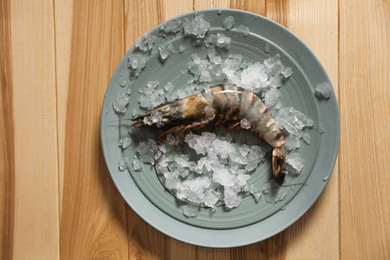 Fresh black tiger shrimp with ice on wooden table, top view