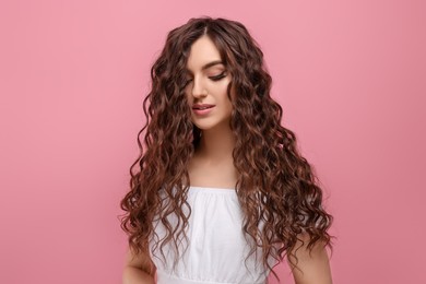 Beautiful young woman with long curly brown hair on pink background