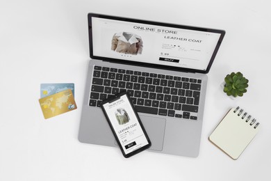 Online store website on laptop screen. Computer, smartphone, notebook, credit cards and houseplant on white background, flat lay