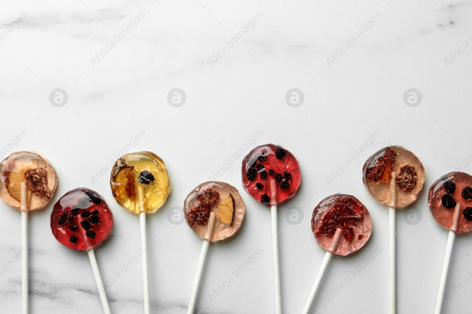 Photo of Sweet colorful lollipops with berries on white marble table, flat lay. Space for text