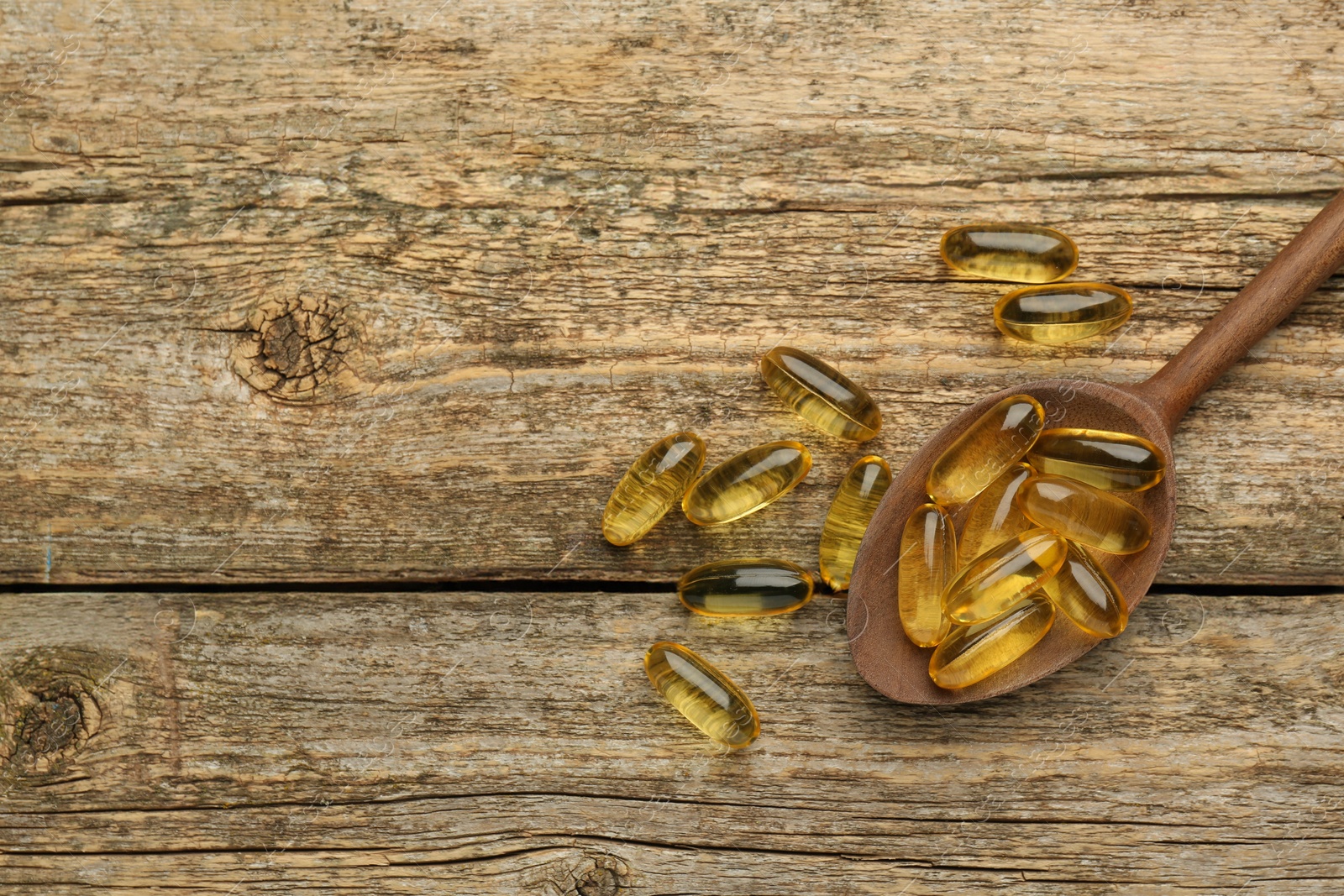 Photo of Vitamin capsules in spoon on wooden table, top view. Space for text