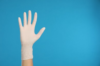 Photo of Doctor wearing medical gloves on light blue background, closeup. Space for text