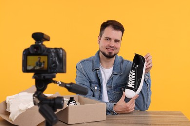 Smiling fashion blogger showing sneaker while recording video at table against orange background