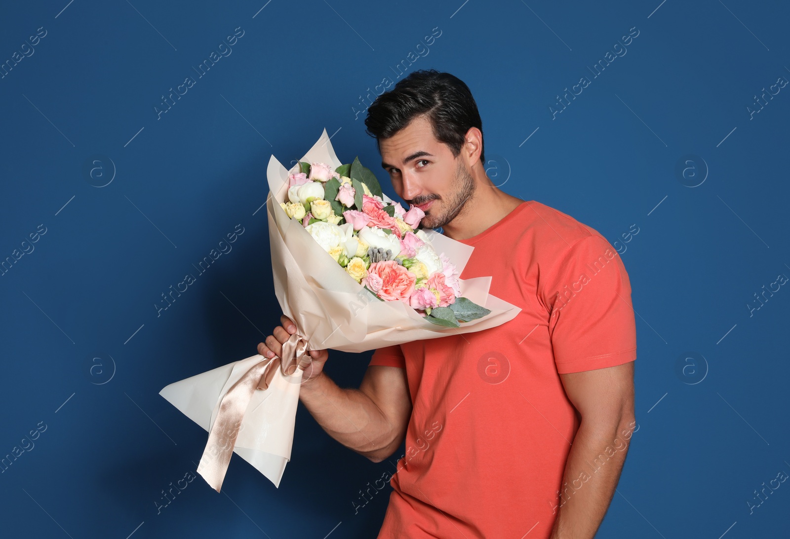 Photo of Young handsome man with beautiful flower bouquet on blue background