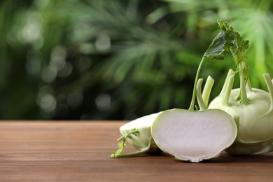Photo of Whole and cut kohlrabi plants on wooden table. Space for text