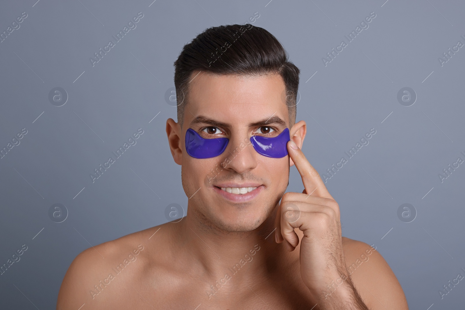 Photo of Man applying blue under eye patch on grey background