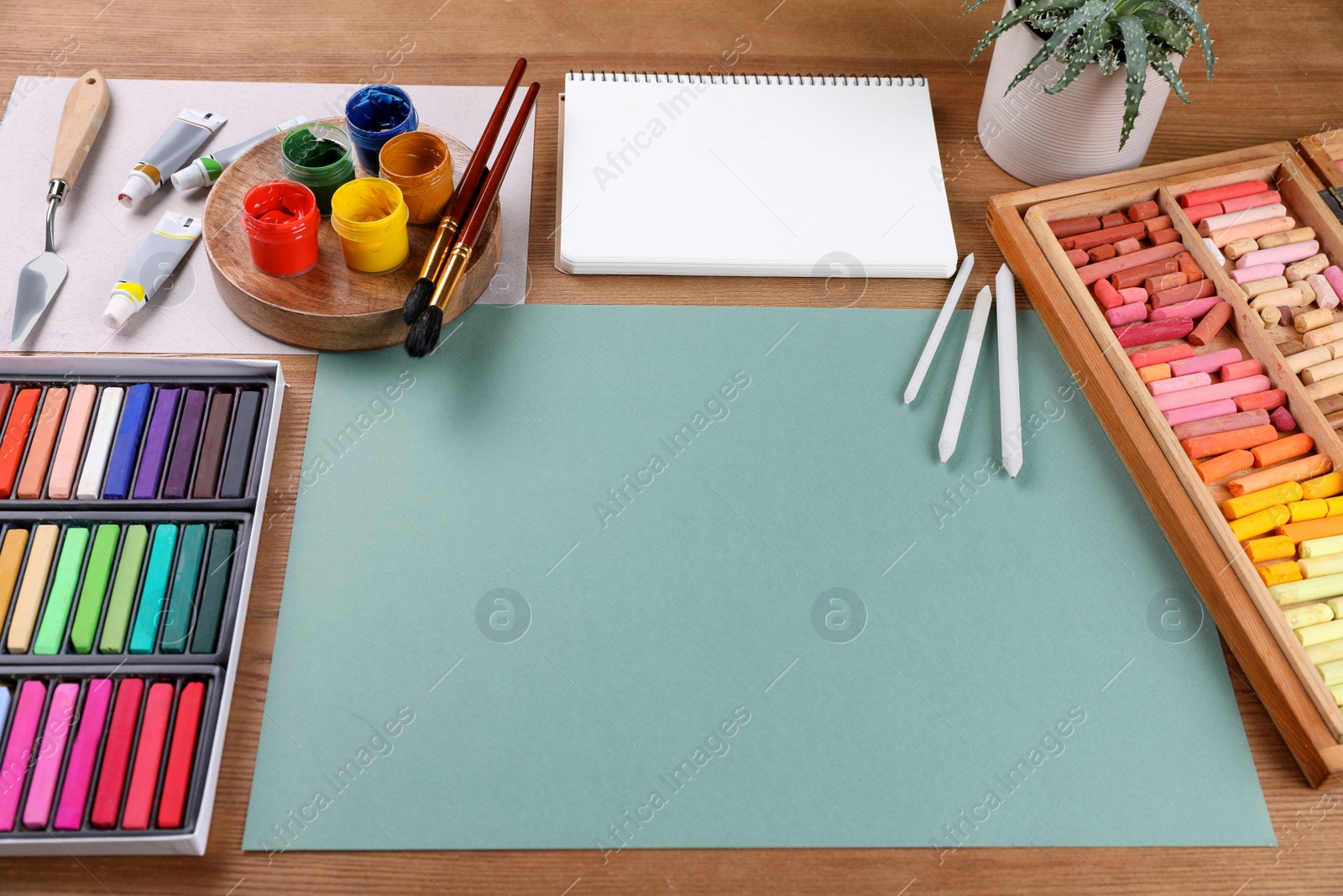 Photo of Blank sheet of paper, colorful chalk pastels and other drawing tools on wooden table. Modern artist's workplace