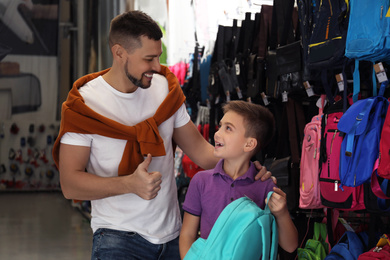 Photo of Little school boy with father choosing backpack in supermarket