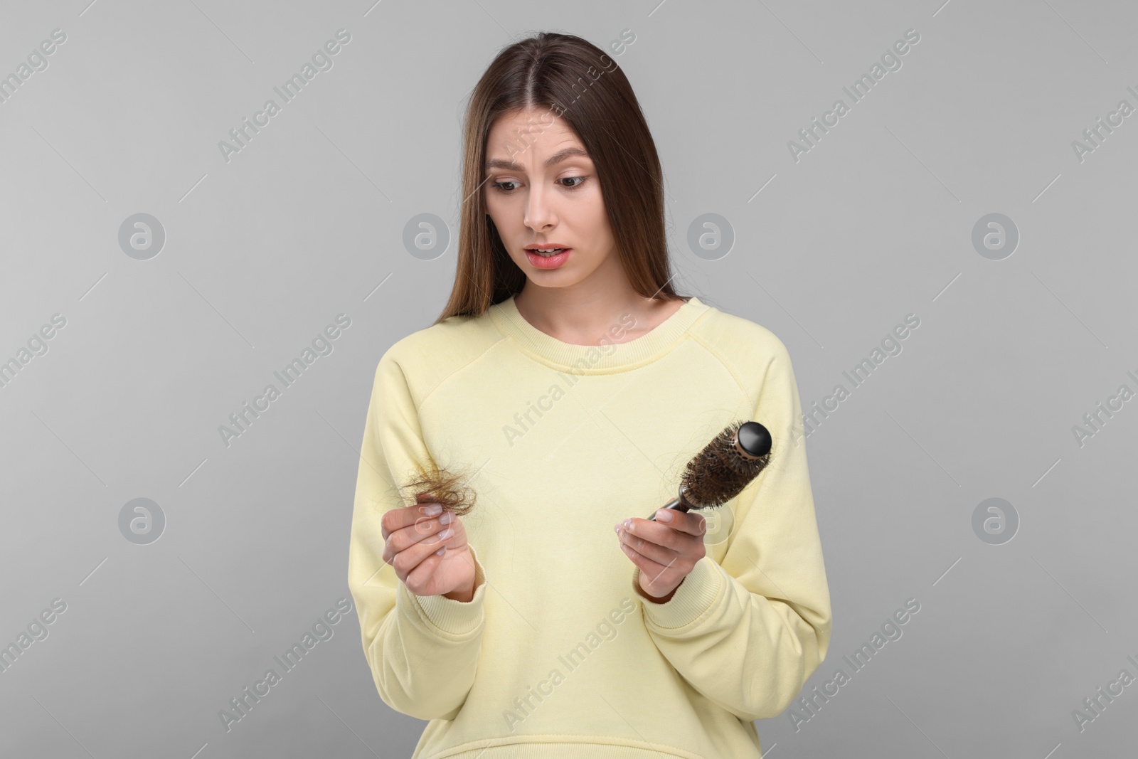 Photo of Emotional woman holding brush with lost hair on light grey background. Alopecia problem