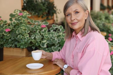 Portrait of beautiful senior woman drinking coffee at table in outdoor cafe