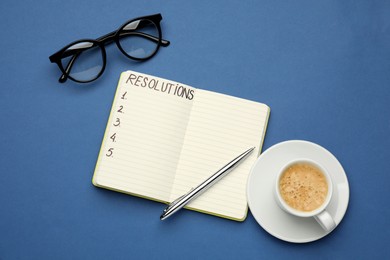 Photo of Making new year's resolutions. Notebook, cup of coffee and glasses on blue background, flat lay