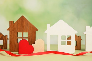 Photo of Long-distance relationship concept. House models, decorative hearts and red ribbon on light green background