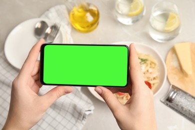 Chroma key compositing. Woman holding smartphone with green screen at table indoors, closeup. Mockup for design