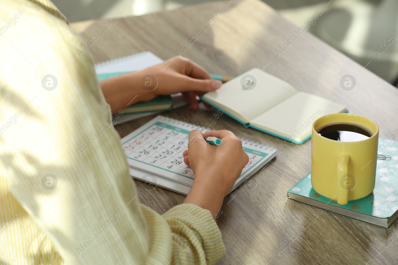 Photo of Woman marking date in calendar at wooden table, closeup