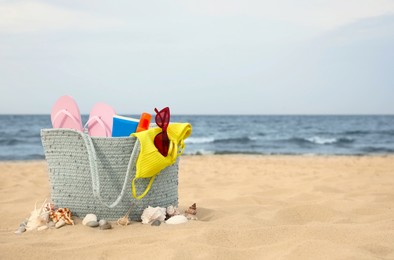 Photo of Bag and different beach objects on sand near sea, space for text