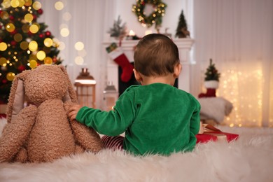 Photo of Baby in elf costume with toy bunny at home, back view. Christmas time