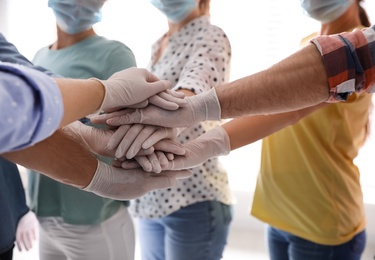 People in white medical gloves stacking hands on light background, closeup