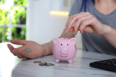 Photo of Woman putting money into piggy bank at marble table indoors, closeup