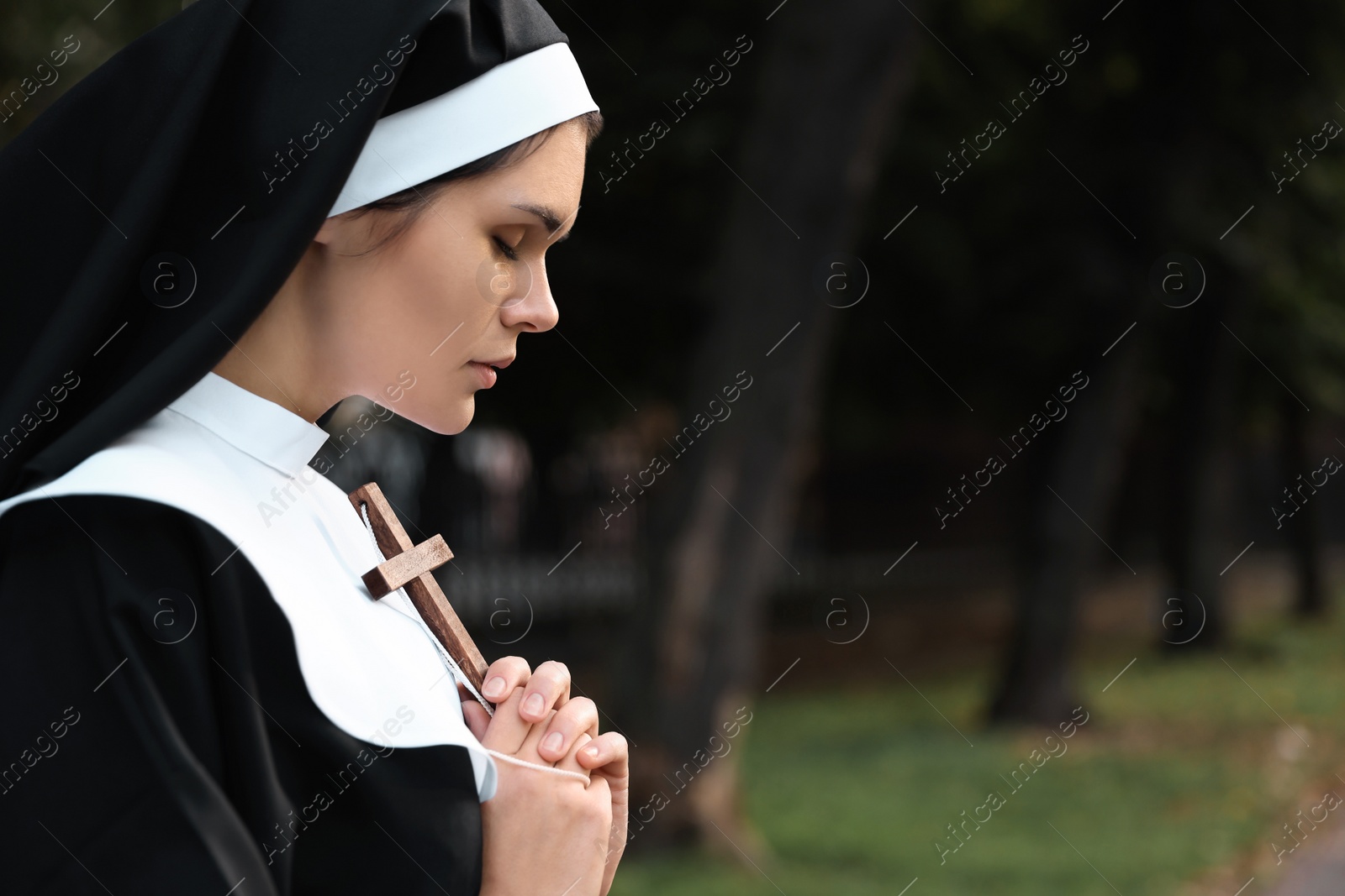 Photo of Young nun with Christian cross in park outdoors, space for text