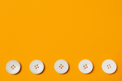 Photo of Line of white buttons on orange background, flat lay. Space for text