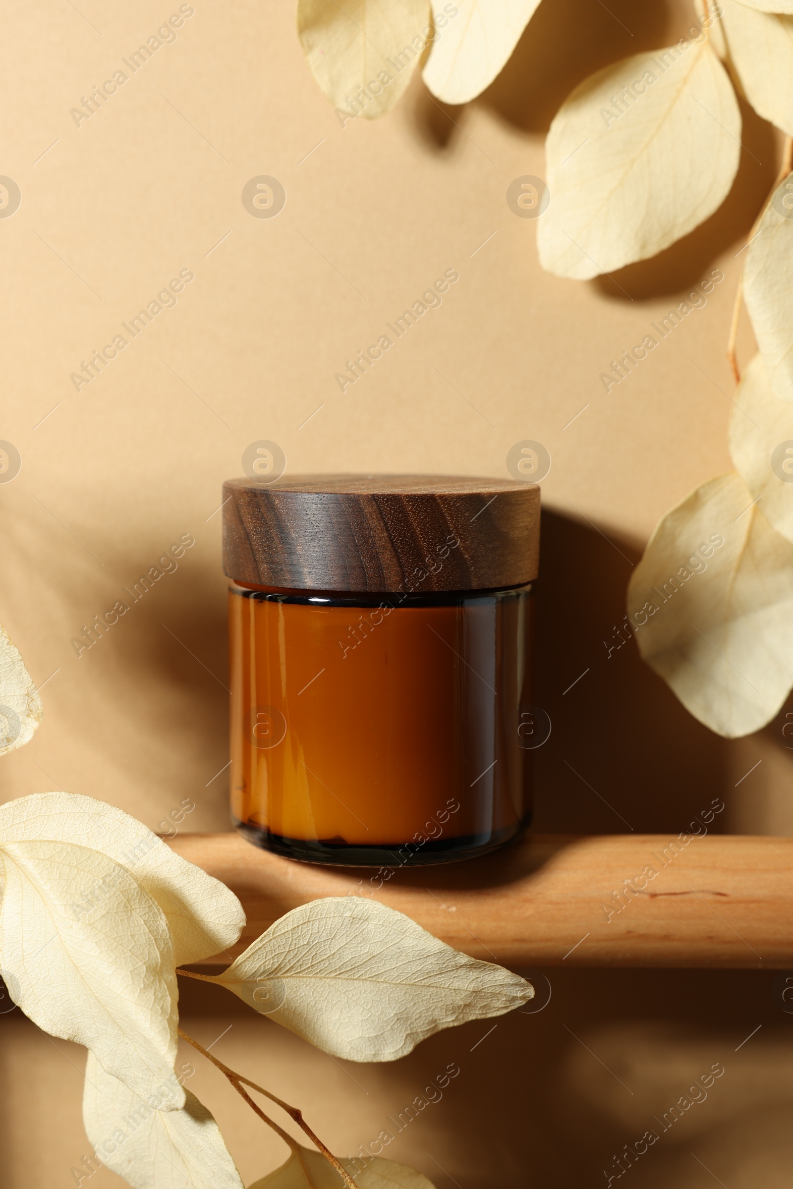 Photo of Jar of luxury cream and dried leaves on dark beige background