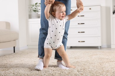 Photo of Mother supporting her baby son while he learning to walk on carpet at home