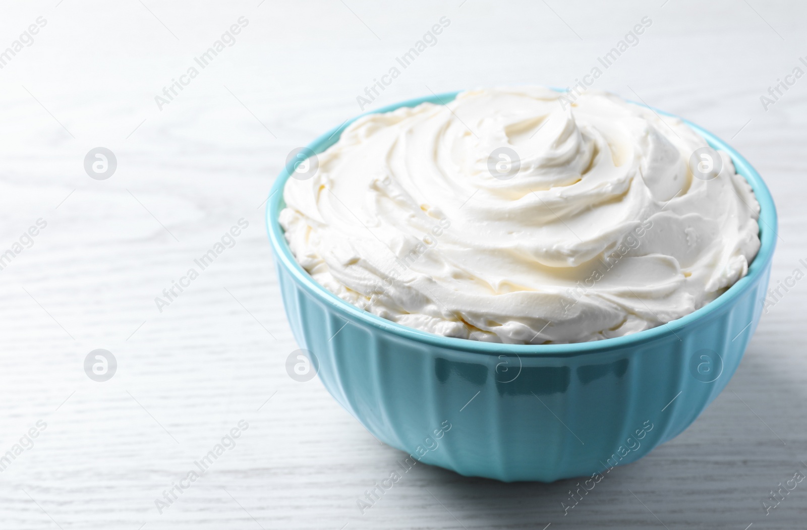 Photo of Bowl of tasty cream cheese on white wooden table, space for text