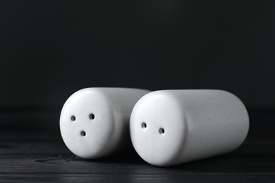 Photo of Pepper and salt shakers on black wooden table, closeup