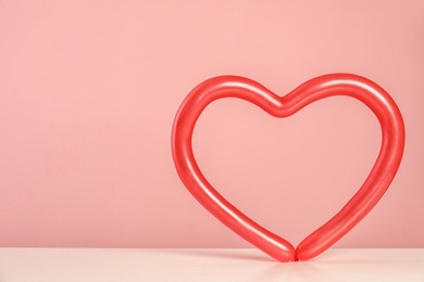 Photo of Heart figure made of modelling balloon on table against color background. Space for text