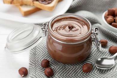 Jar with chocolate paste and nuts on white table, closeup