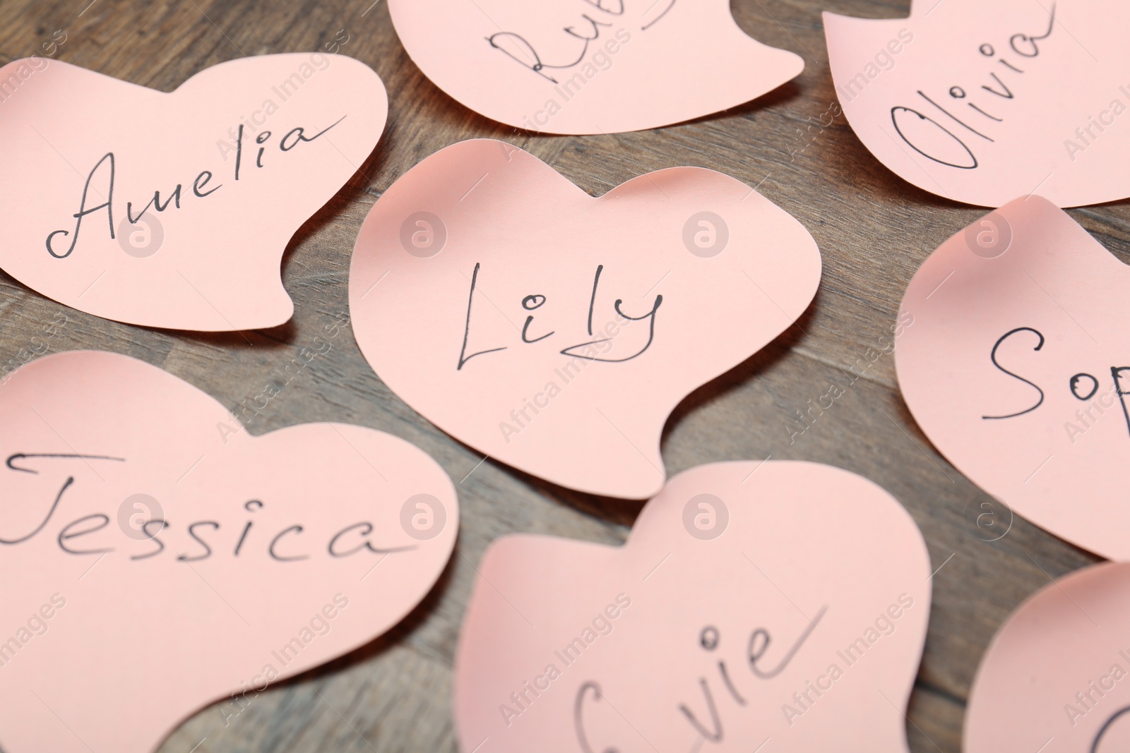 Photo of Paper stickers with different names on wooden table, closeup. Choosing baby's name