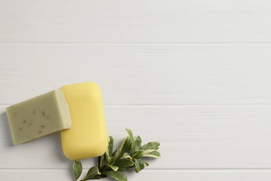 Photo of Soap bars and green plant on white wooden table, flat lay. Space for text