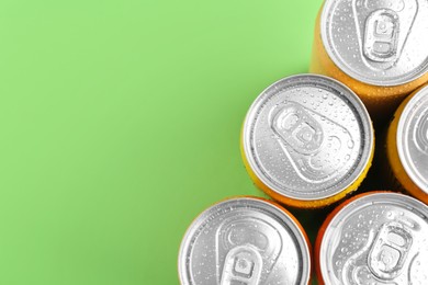 Photo of Energy drinks in wet cans on green background, top view. Space for text