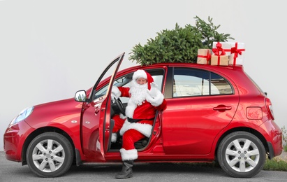 Authentic Santa Claus in car with gift boxes and Christmas tree, view from outside