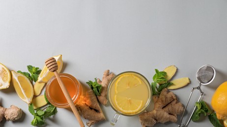 Photo of Glass of aromatic ginger tea and ingredients on light grey background, flat lay. Space for text