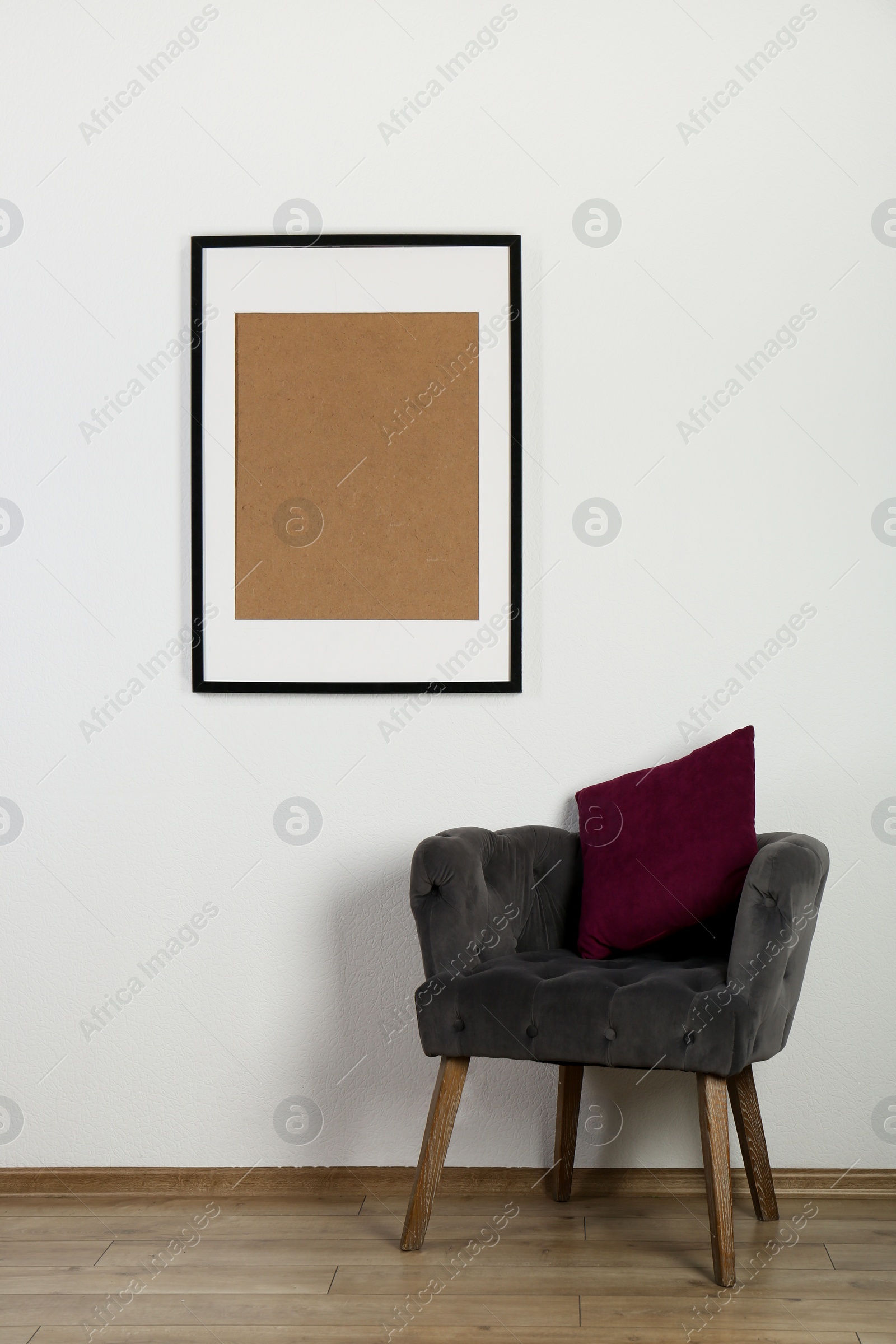 Photo of Comfortable armchair, cushion and picture frame on wall indoors. Interior element