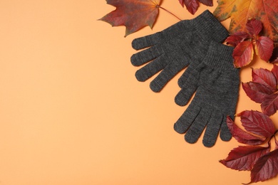 Photo of Stylish woolen gloves and dry leaves on pale orange background, flat lay. Space for text