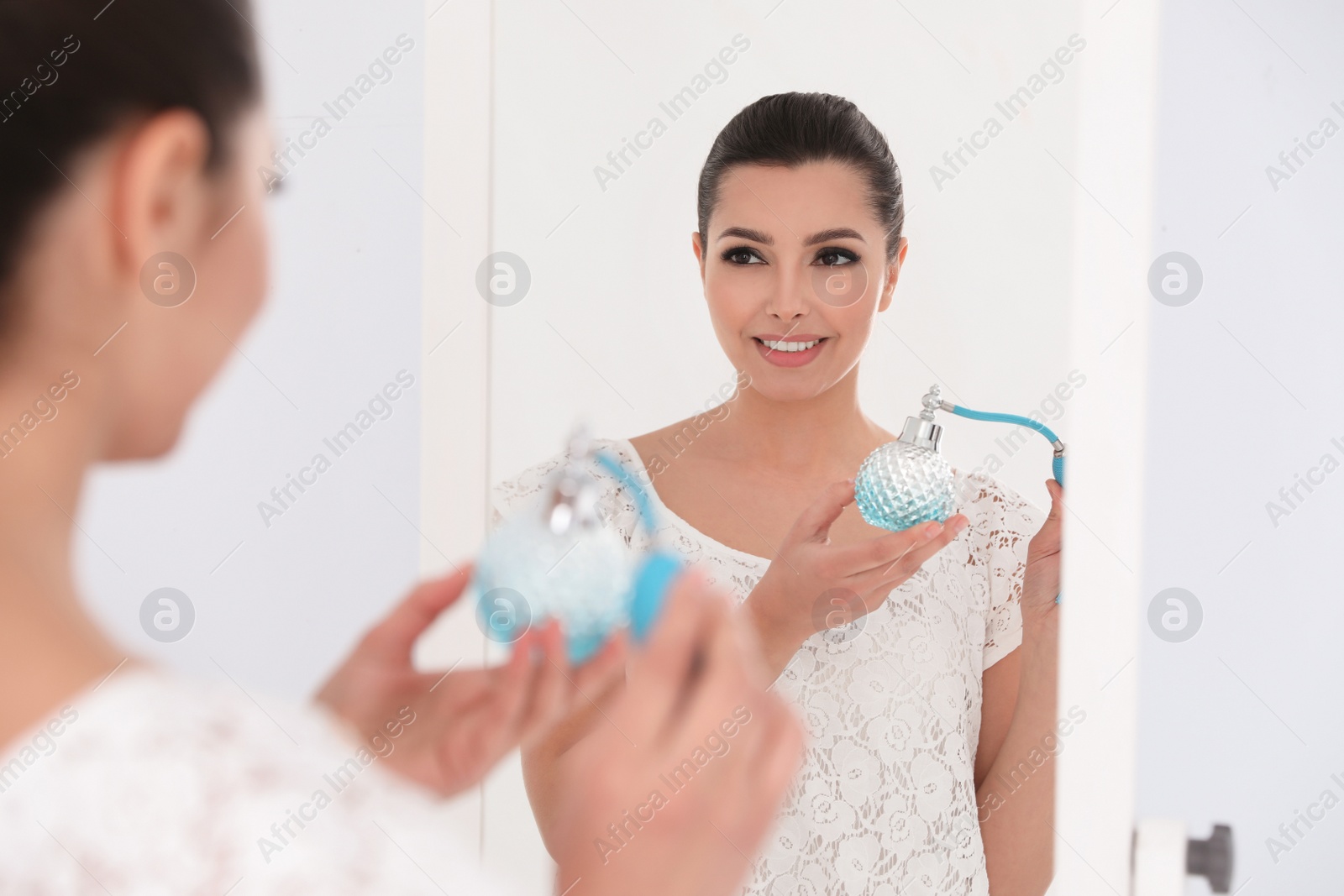 Photo of Young woman with bottle of perfume near mirror indoors