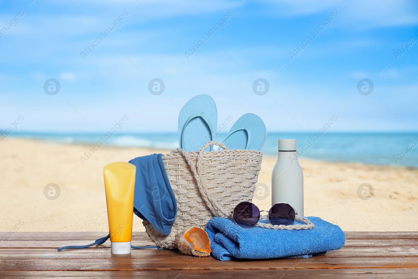 Image of Stylish bag and other beach accessories on wooden table near sea