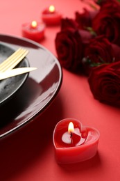 Place setting with heart shaped candles and bouquet of roses on red table, closeup. Romantic dinner