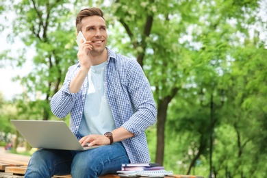 Photo of Young man with laptop talking on phone in park