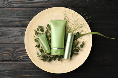 Set of cosmetic products and plants on dark wooden table, top view