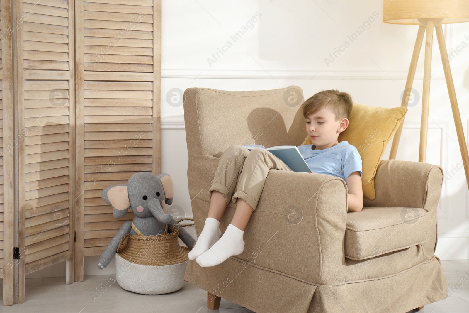 Photo of Little boy reading book in armchair at home