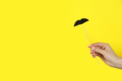 Photo of Woman with fake paper mustache on yellow background, closeup. Space for text