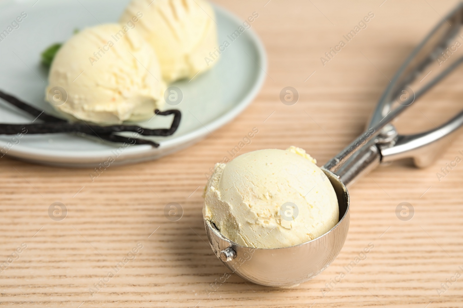 Photo of Scoop with delicious vanilla ice cream near plate on wooden table