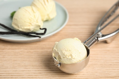 Scoop with delicious vanilla ice cream near plate on wooden table